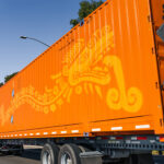 "Remolque porta contenedor de 40 pies en tránsito para montaje de tienda móvil Contenedor montado en remolque funcionando como tienda pop-up para activación de marca Remolque para contenedor siendo transportado para activación comercial en vía pública"